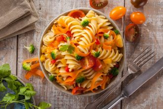 Fusilli pasta with colorful tomatoes, carrots and broccoli on a white wooden table Italian cuisine.