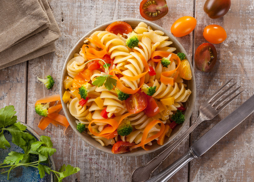 Fusilli pasta with colorful tomatoes, carrots and broccoli on a white wooden table Italian cuisine.