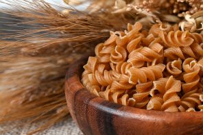 Bowl of wholegrain pasta spirals or fusilli, over light wooden background. Copy space