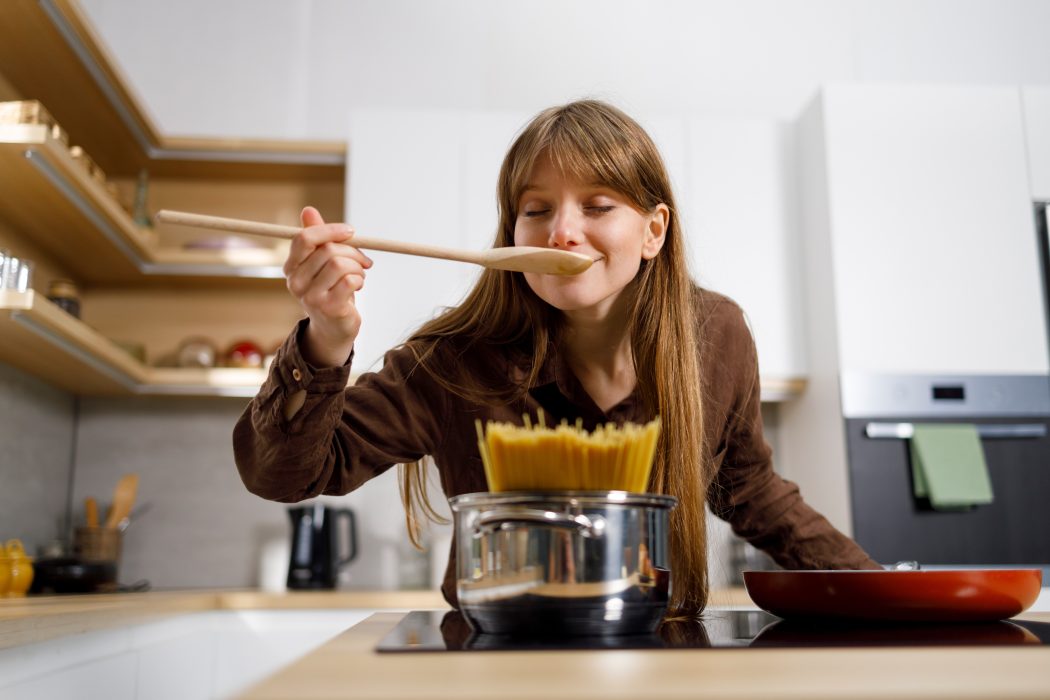 Cheerful girl is tasting food while cooking in kitchen at home